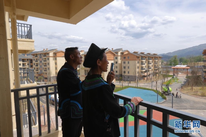 在四川省昭覺縣城易地扶貧搬遷安置點南坪社區(qū)，剛搬遷到新家的“懸崖村”村民莫色達體夫婦在陽臺給親戚打電話（2020年5月13日攝）。新華社記者 江宏景 攝