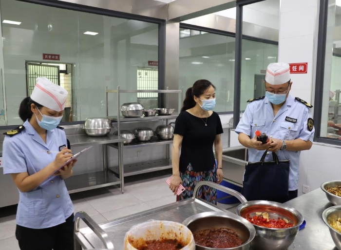 圖為執(zhí)法人員在檢查學校食堂加工制作情況。
