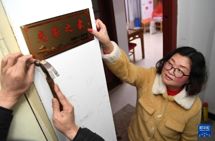 合肥市包河區(qū)常青街道工作人員在居民魏松梅（右）家門口懸掛“光榮之家”牌（2019年1月14日攝）。新華社記者 劉軍喜 攝