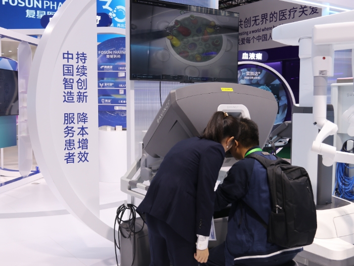 圖為復(fù)星醫(yī)藥展臺工作人員正在指導(dǎo)觀眾體驗國產(chǎn)達(dá)芬奇XI手術(shù)系統(tǒng)。（郭婷 攝） 